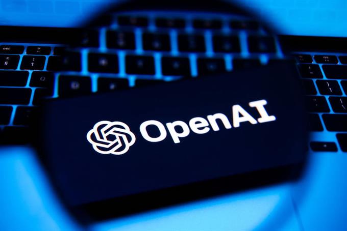 Magnifying glass held over smart phone displaying OpenAI logo